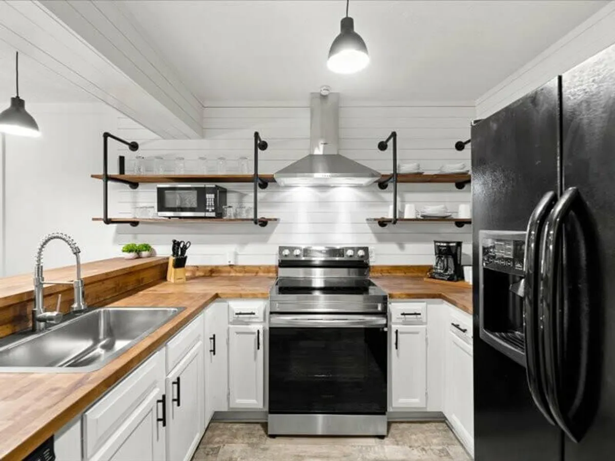 A well-equipped kitchen with a stainless steel stove, wooden countertop, open shelving, a double sink, and a black refrigerator. The warm lighting and inviting layout create a welcoming environment for cooking and gathering.
