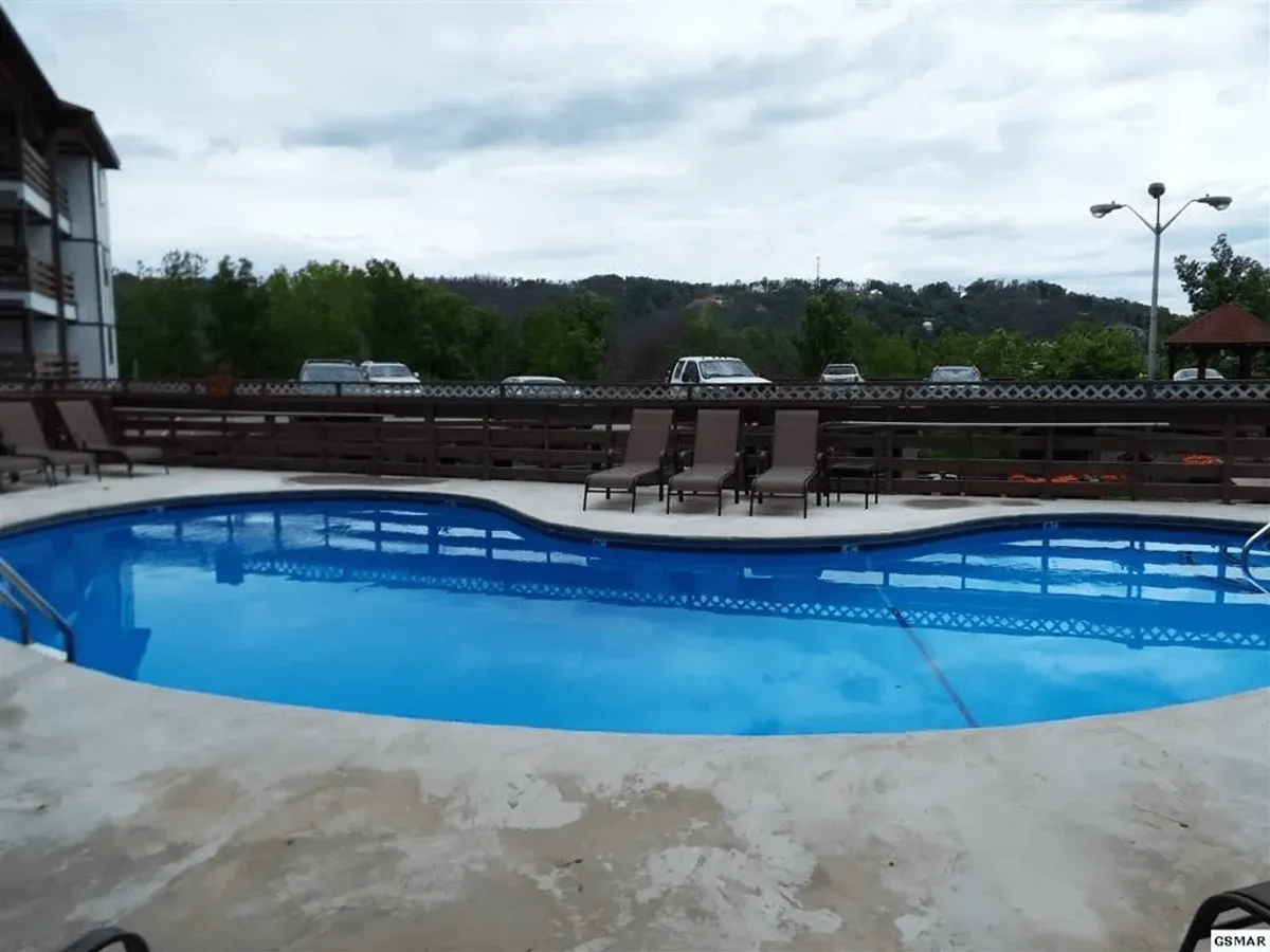 This inviting exterior image features a sparkling swimming pool surrounded by lounge chairs and lush greenery. The tranquil setting is ideal for both cooling off after a day of mountain adventures and relaxing with a book in the sun. The scene conveys the sense of leisure and community central to condo living.