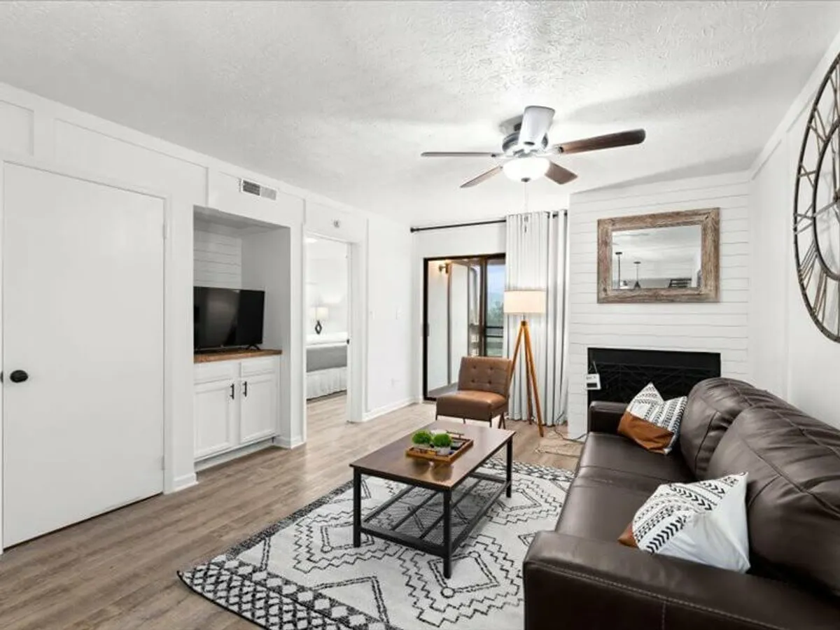 A cozy living room scene with a leather sofa, coffee table adorned with plants, a TV unit, and a large mirror reflecting the room's brightness. The floor lamp and indoor greenery add warmth, while modern accents create a fresh, inviting atmosphere.