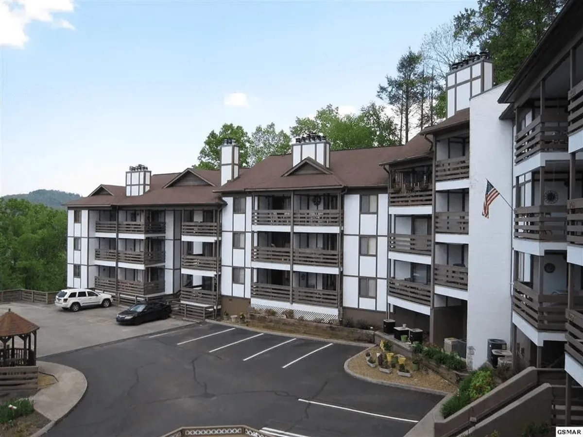 This image features the condo building with balconies overlooking landscaped gardens and a parking area. Residents can be seen relaxing and socializing, illustrating the building's inviting community atmosphere and its central location within reach of local attractions.