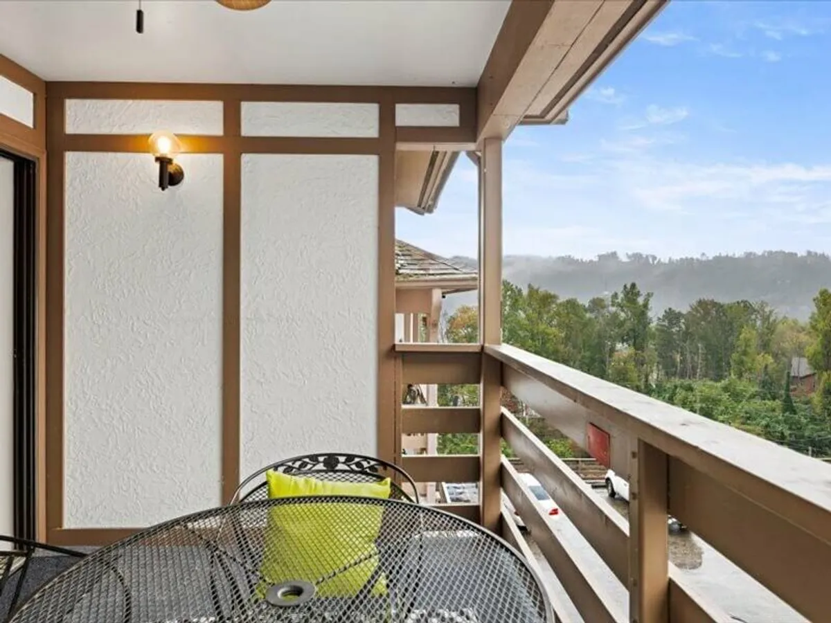This image shows a private balcony with a bistro table and chairs, accented by a bright yellow cushion and a railing that overlooks the natural landscape. The tranquil setting is ideal for sipping coffee or enjoying quiet moments with a partner, with hints of sunrise or sunset light enhancing the romantic atmosphere.