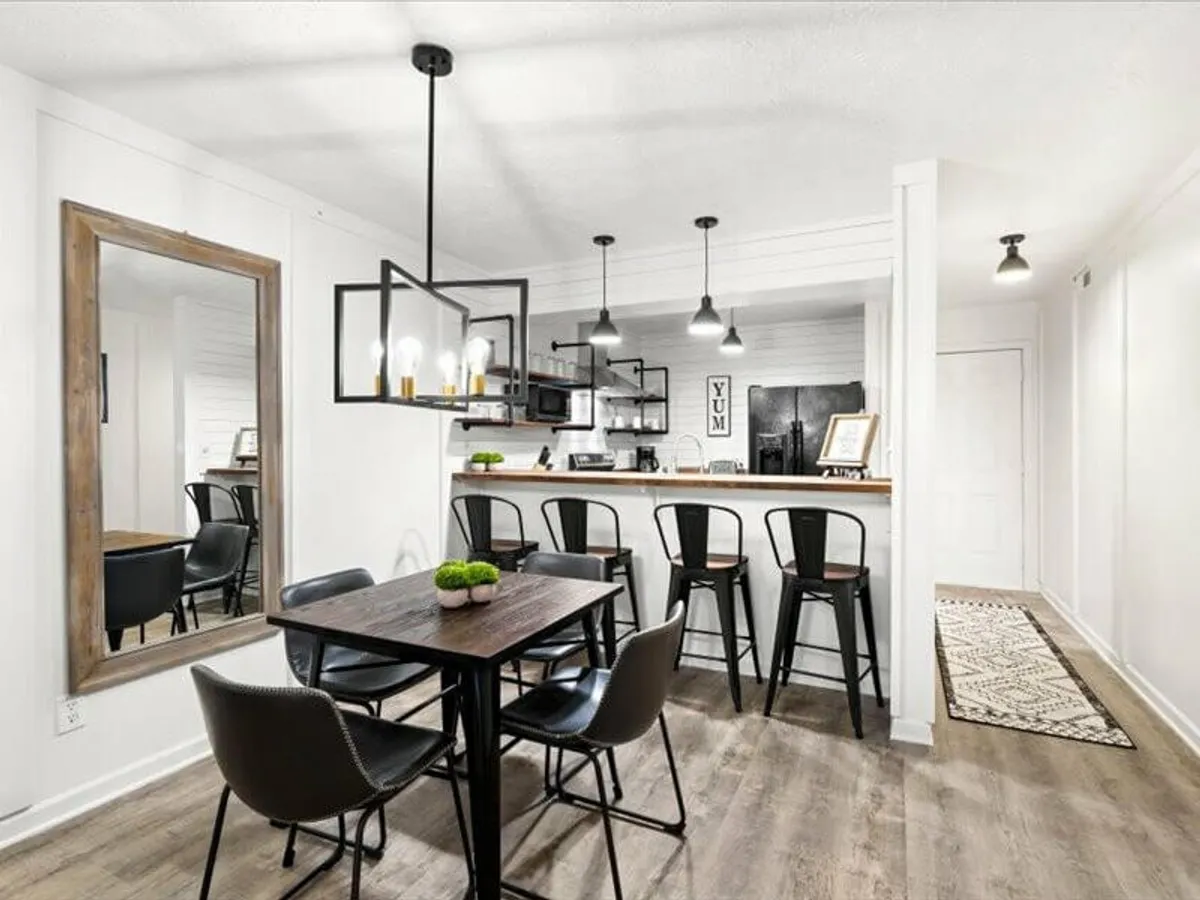 The image showcases a contemporary, open-concept dining and kitchen area with a polished dining table, inviting bar stools at a gleaming kitchen counter, and a large wall mirror that reflects warm light. The space feels modern yet cozy—ideal for family meals, casual gatherings, or entertaining after a day of exploring Gatlinburg and the Smoky Mountains.
