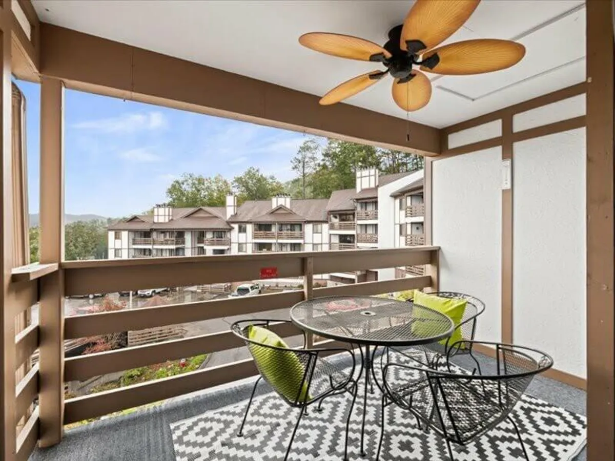 An inviting outdoor dining table sits on a covered balcony, with a ceiling fan overhead and views of surrounding buildings and natural scenery. The setting is ideal for relaxing, sharing meals, and recapping the day’s adventures.